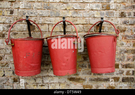 Three red old fashioned fire buckets hanging on hooks on an old wall Stock Photo
