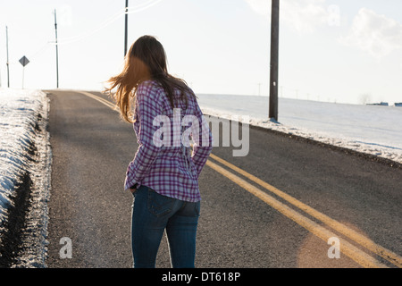 Young woman walking up remote road in winter Stock Photo