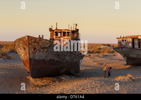 A father and granddaughter on a sunset walk in the ship graveyard near the former port of Moynaq on the Aral Sea, Uzbekistan. Stock Photo