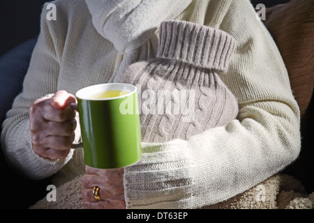 Senior woman holding mug and hot water bottle Stock Photo