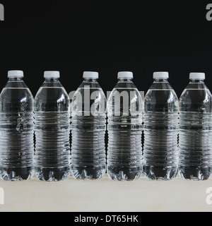 Row of clear, plastic water bottles filled with filtered water in a row, on a black background. Stock Photo