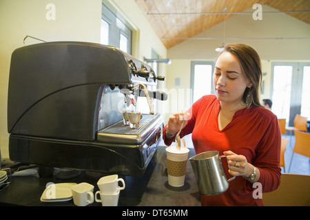 A young woman making coffee using a large coffee machine. Pouring frothed milk onto a cup. Stock Photo