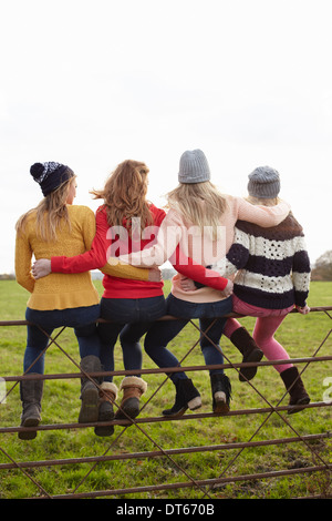 Rear view of four teenage girls sitting on gate Stock Photo