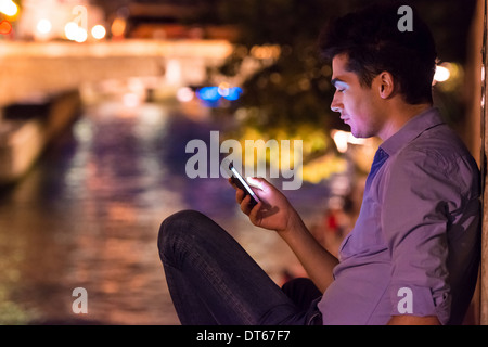 Young man looking at smartphone at night, Paris, France Stock Photo