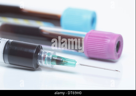 Disposable plastic medical syringe and color coded tubes containing synthetic blood samples. Blue top - buffered sodium Stock Photo