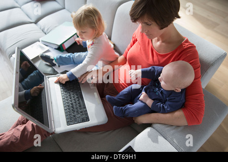 Mother, baby boy and female toddler using laptop on sofa Stock Photo