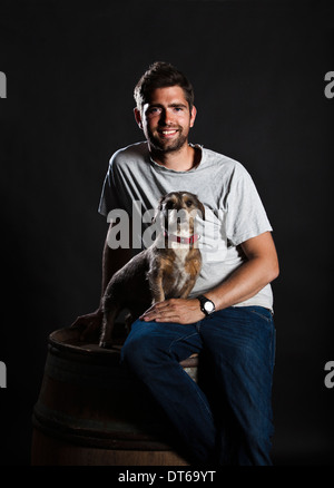 Portrait of winemaker and his dog sitting on wine barrel Stock Photo