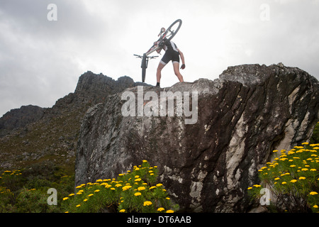 Young man carrying mountain bike on top of rock formation Stock Photo