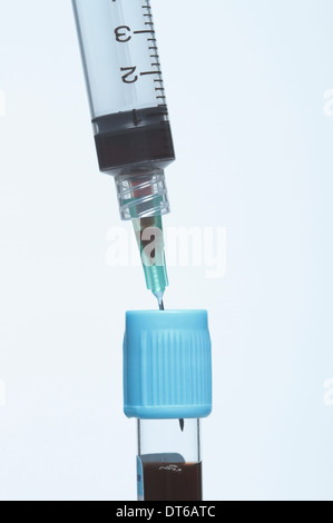 Disposable plastic medical syringe inserted into blue blood tube containing synthetic blood sample. Stock Photo