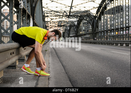 Young male runner tying shoelace on bridge Stock Photo