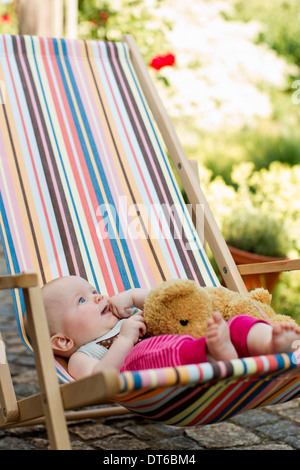 Baby girl sitting on deck chair with teddy bear Stock Photo