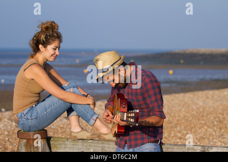 Young couple on beach, man playing guitar Stock Photo