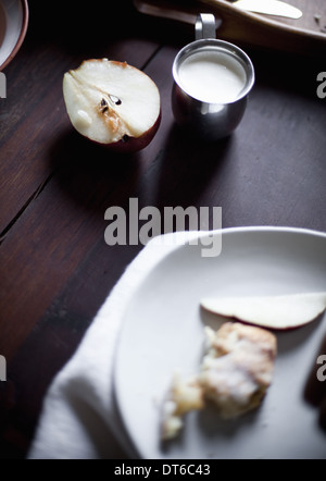 A pear fruit cut open, and sliced. Served on a white china plate. A jug of cream. A breakfast table. Stock Photo
