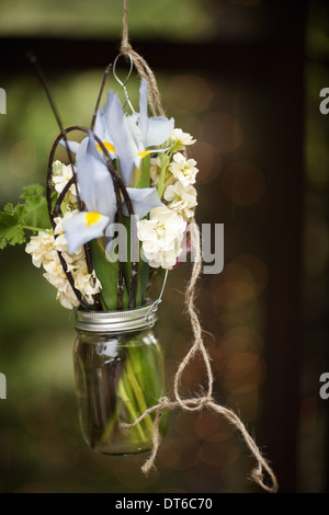 A small glass jar hanging from a wire, with iris and scented stock flowers. A floral decoration. Stock Photo