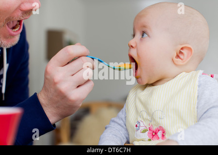 Father spoon feeding baby daughter Stock Photo