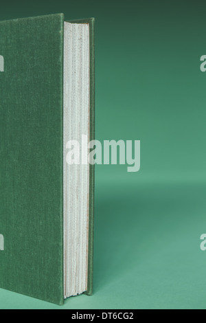 A hard cover book with a green cover, and white paper page edges, upright on a green background. Stock Photo