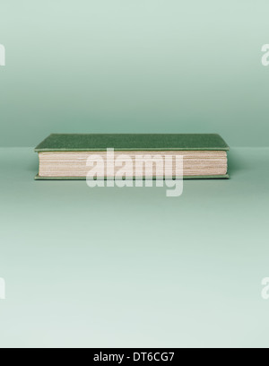A hard cover book with a green cover, and white paper page edges, lying horizontal on a pale green background. Stock Photo