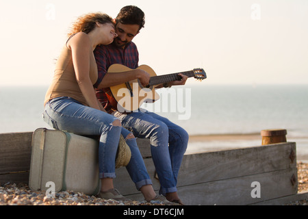 Young couple on beach, man playing guitar Stock Photo