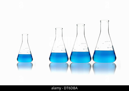 Conical glass scientific flasks holding blue liquids. Lined up in size order, with one set apart. Stock Photo