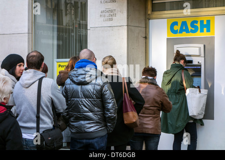 Shoppers waiting in queue to collect money from ATM cash dispenser of bank in shopping street in winter Stock Photo