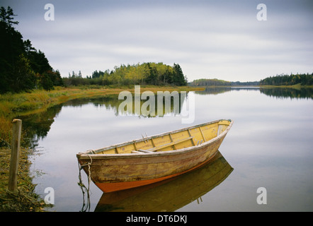 A small wooden dory or rowing boat moored on flat calm water, in Savage harbour on Prince Edward Island in Canada.