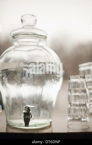 Drinking water in a large clear glass container. A stack of glasses. Pure chilled water. Stock Photo