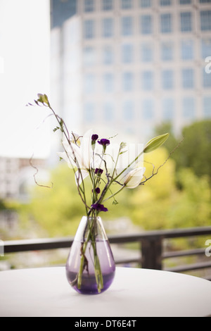 A table on a terrace in the city. A vase of flowers. Small purple flowers, and white lily and orchid blooms. Stock Photo