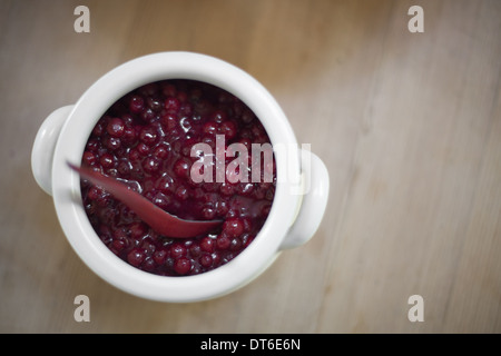 A white pottery bowl, full of fresh cranberries with a matching spoon. A relish or sauce. Stock Photo