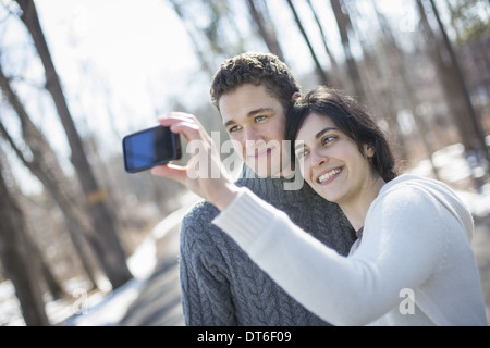 A couple outdoors on a snowy day. Woman holding a camera phone, taking photographs at arms length. Stock Photo