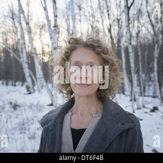 A mature woman with curly read hair, wearing a coat. Standing on a snowy path through woodland. Stock Photo