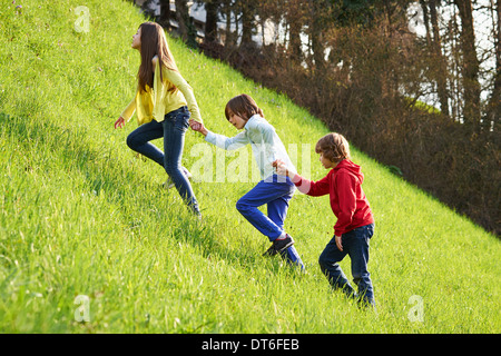 Sister and younger brothers climbing up grassy field Stock Photo