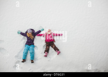 Two sisters playing, making snow angels in snow Stock Photo