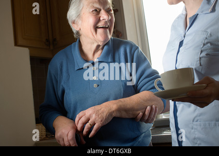 Personal care assistant carrying cup of tea for senior woman Stock Photo