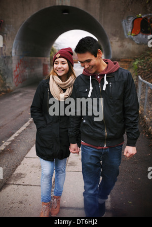 Loving young couple walking on a street smiling. Mixed race couple walking on sidewalk. Stock Photo