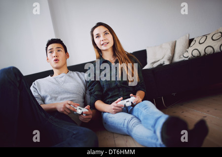 Young couple playing video games together while sitting in their living room. Mixed race teenage couple holding video game. Stock Photo