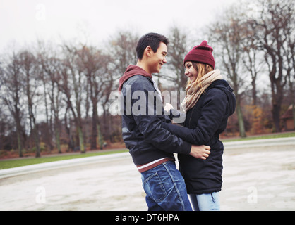 Handsome young man and beautiful woman standing together looking at each other smiling. Teenage mixed race couple in love Stock Photo