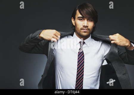 Portrait of young businessman wearing coat. Mixed race male model getting dressed against black background. Stock Photo