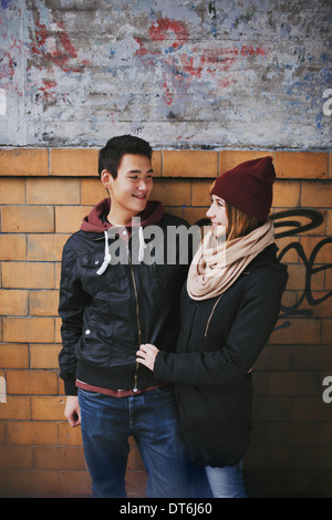 Happy young couple looking at each other against a wall. Teenage asian man and woman in love spending time together outdoors. Stock Photo