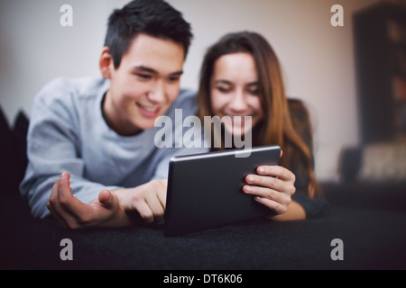 Teenage couple using digital tablet. Focus on tablet PC. Young man and woman using touch screen computer at home. Stock Photo