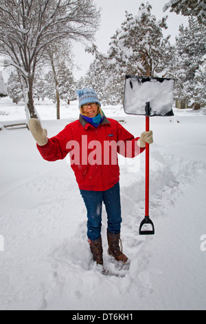 A woman shoveling snow from her deck or front porch at a country house in central Oregon during a heavy snow storm. Stock Photo