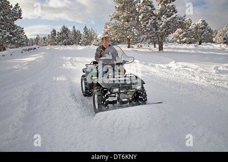 A senior citizen plows snow with an ATV, all terrain vehicle, after a major snow storm in central Oregon. Stock Photo