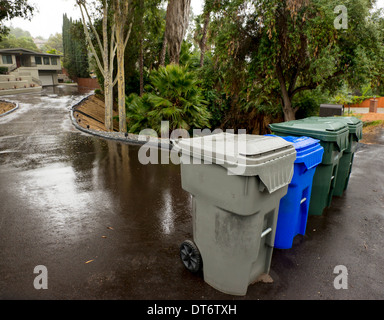 Suburban street shot of trash, recycle and garden trimmings bins set out on a rainy pick-up day with home in background. Stock Photo