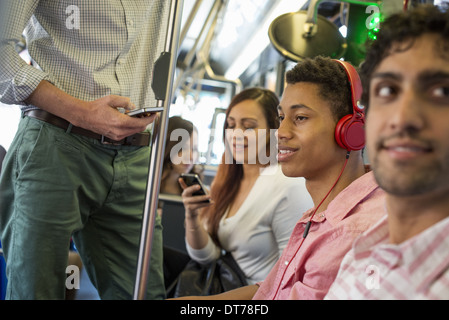 men and women on a city bus, in New York city. A man with headphones on. A man and a woman checking their smart phones. Stock Photo