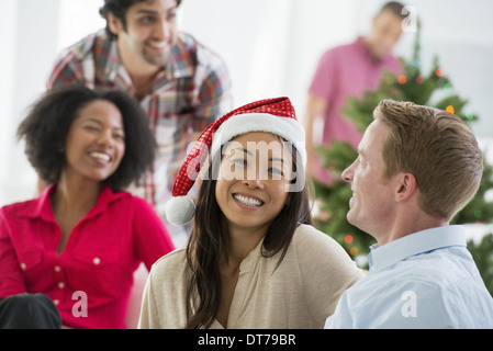 A woman wearing a red and white Father Christmas hat.  At home. A decorated Christmas tree. Stock Photo