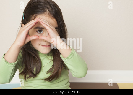 A young girl with long brown hair holding her hands up to her face, and peeping through her hands. Stock Photo