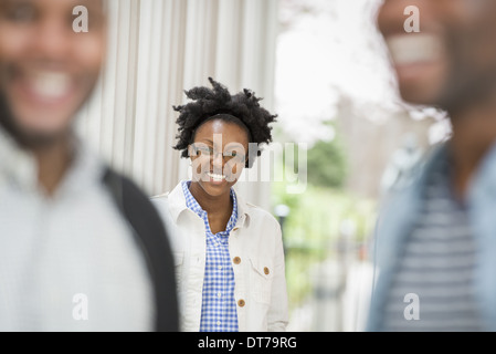 A woman looking at the camera, with two men in the foreground. Stock Photo