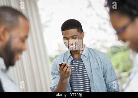 A young man checking his phone, behind a couple in the foreground. Stock Photo