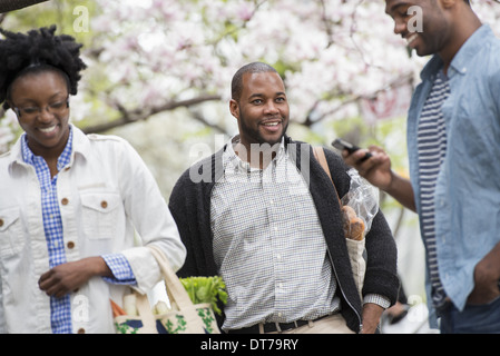 Three people in the park. One man checking his phone. Stock Photo