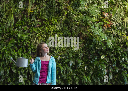 A young girl standing in front of a wall covered with ferns and climbing plants. Stock Photo