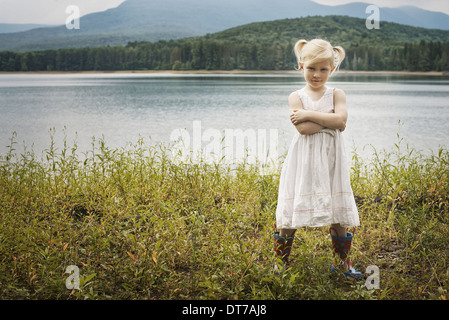 A young girl in a white summer dress standing with her arms folded looking at the camera Woodstock New York USA Stock Photo